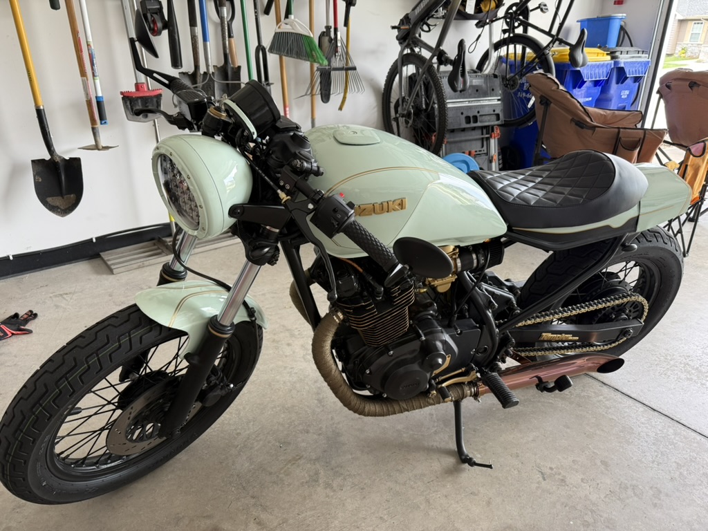 Conner's mint-green Suzuki cafe racer with gold accents and a diamond-stitched seat, parked in the garage