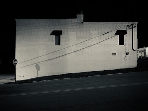 Black-and-white night shot of a lit brick wall, power lines, and a stop sign