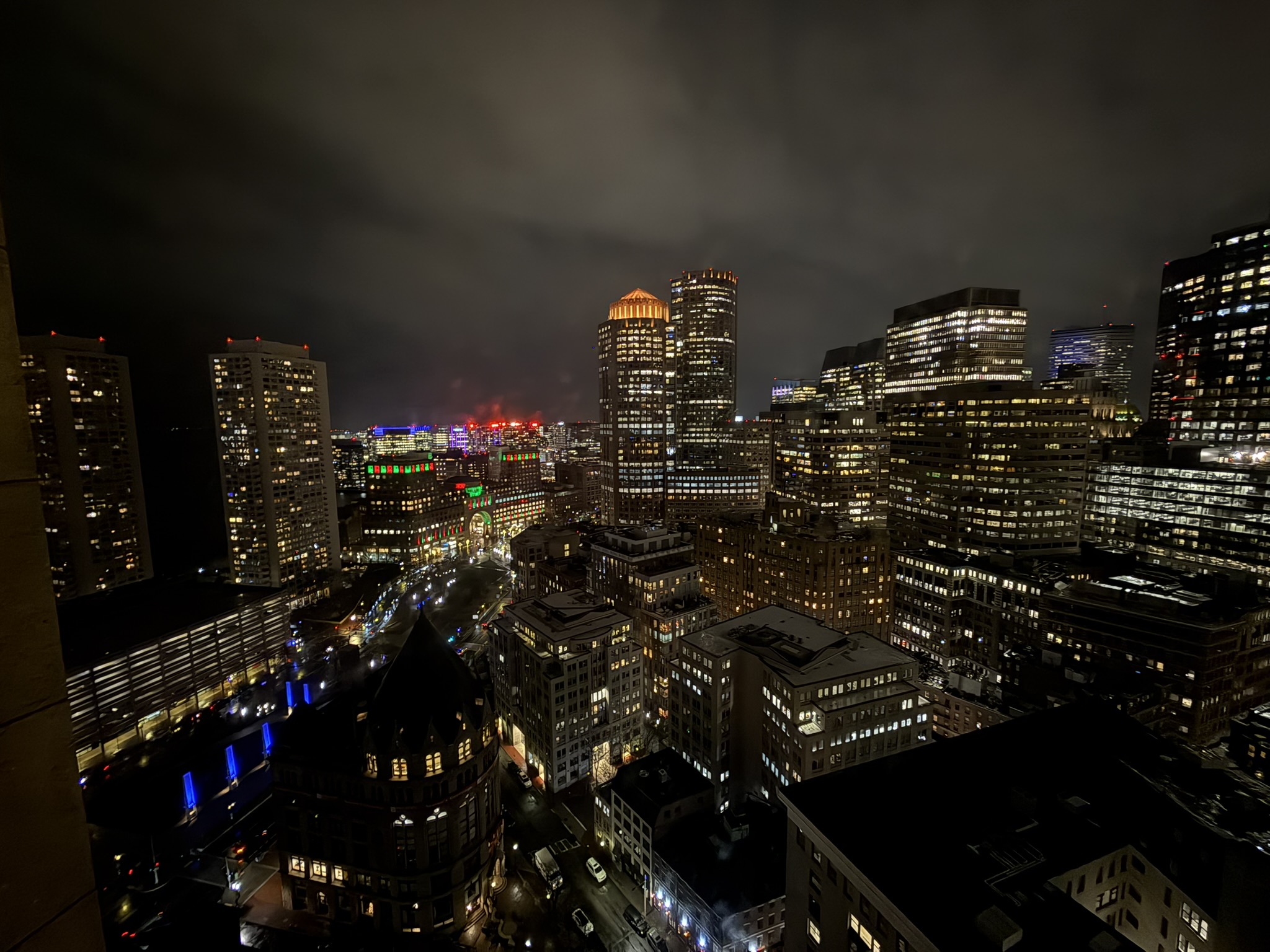 Downtown Boston at night from high above, offices lit under a low cloud ceiling